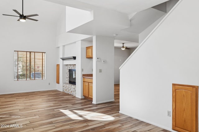 unfurnished living room featuring ceiling fan, light hardwood / wood-style floors, a towering ceiling, and a fireplace