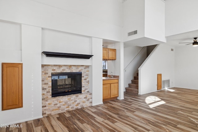 unfurnished living room with ceiling fan, sink, a high ceiling, and light hardwood / wood-style flooring