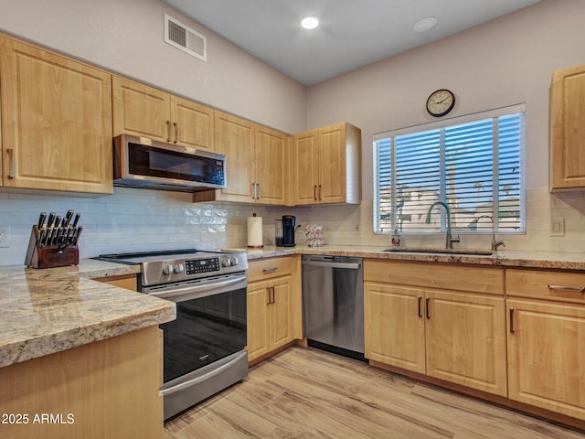 kitchen featuring appliances with stainless steel finishes, light brown cabinets, sink, light wood-type flooring, and light stone counters