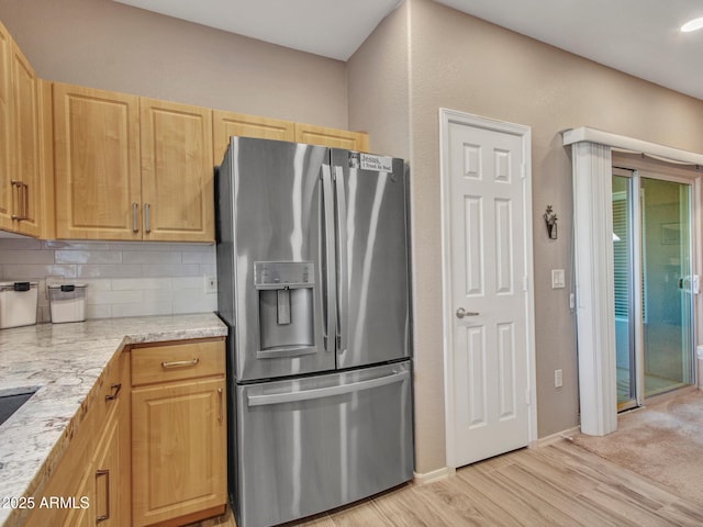 kitchen with stainless steel fridge with ice dispenser, backsplash, light wood-type flooring, light brown cabinetry, and light stone countertops