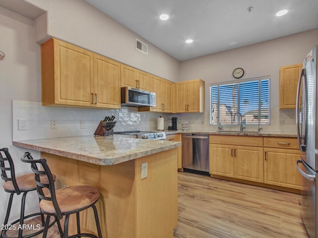 kitchen featuring light hardwood / wood-style floors, a kitchen bar, kitchen peninsula, appliances with stainless steel finishes, and sink