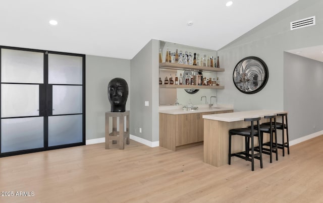 bar with sink, light hardwood / wood-style flooring, and lofted ceiling