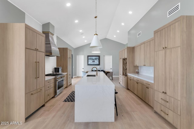 kitchen featuring pendant lighting, high end stainless steel range, wall chimney exhaust hood, light brown cabinetry, and a large island