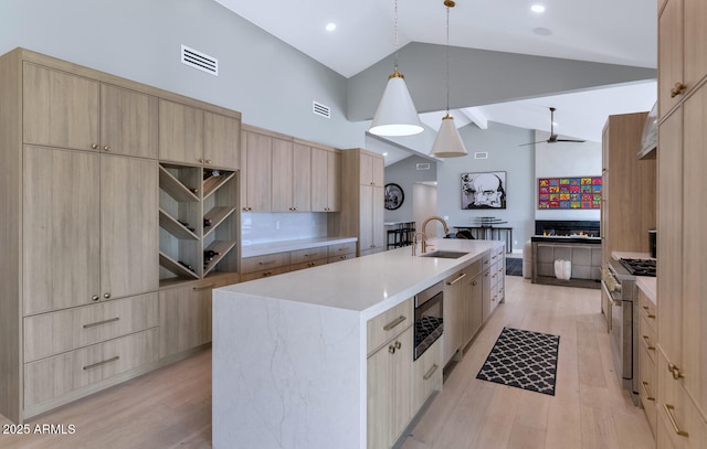 kitchen featuring pendant lighting, an island with sink, light brown cabinetry, sink, and stainless steel stove