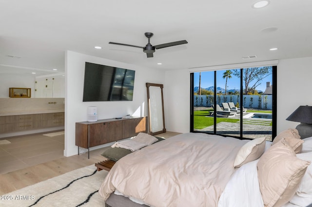 bedroom with ensuite bath, light hardwood / wood-style floors, access to outside, ceiling fan, and expansive windows