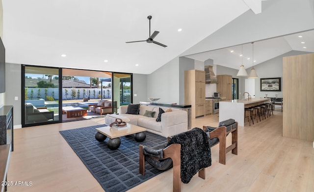 living room with ceiling fan, lofted ceiling, sink, light hardwood / wood-style flooring, and a wall of windows