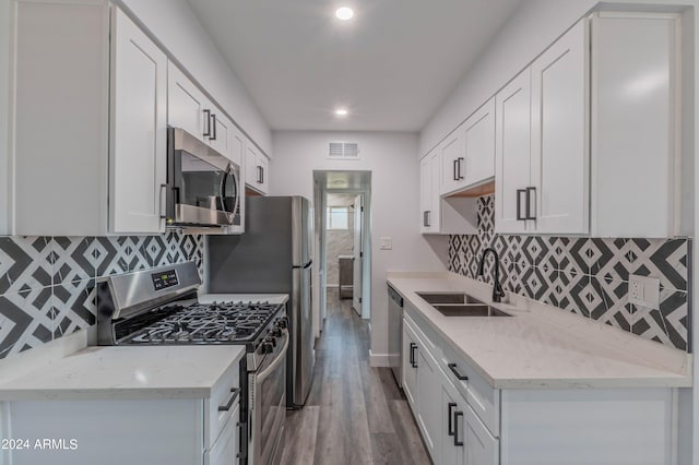 kitchen with white cabinets, light stone countertops, stainless steel appliances, hardwood / wood-style flooring, and sink