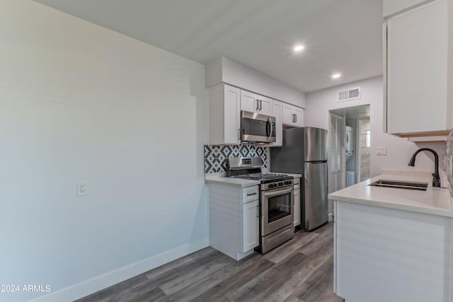 kitchen with sink, wood-type flooring, backsplash, white cabinetry, and stainless steel appliances