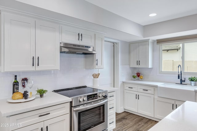 kitchen featuring under cabinet range hood, white cabinetry, light countertops, and electric stove