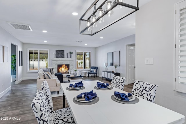 dining room featuring a healthy amount of sunlight, visible vents, a stone fireplace, and dark wood-style flooring