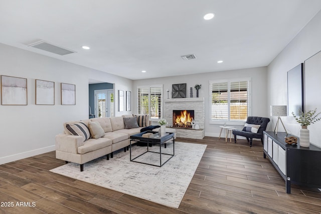 living room with baseboards, visible vents, dark wood-type flooring, and a stone fireplace