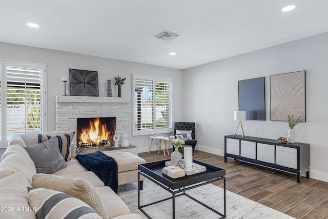 living room featuring plenty of natural light, a fireplace, visible vents, and wood finished floors