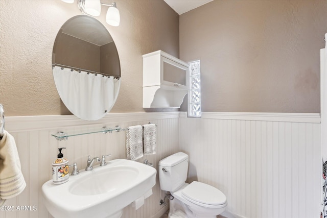bathroom with toilet, a sink, and wainscoting