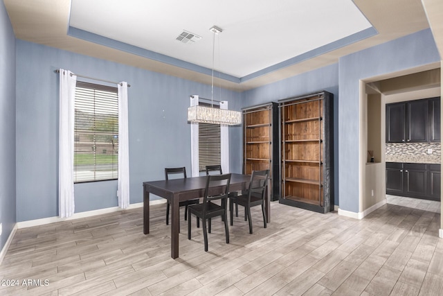 dining room with light hardwood / wood-style floors, an inviting chandelier, and a tray ceiling