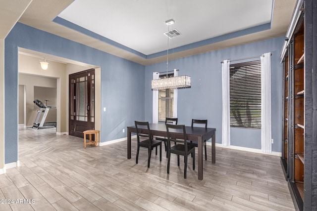 dining room with a tray ceiling, a healthy amount of sunlight, and an inviting chandelier