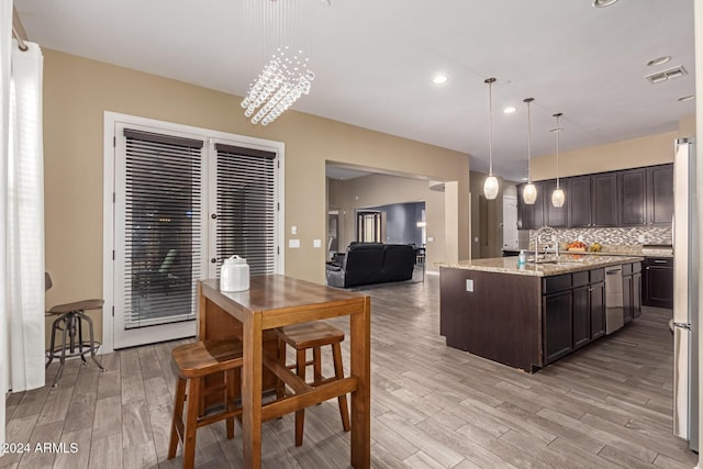 kitchen with light stone countertops, tasteful backsplash, decorative light fixtures, dark brown cabinets, and a center island with sink