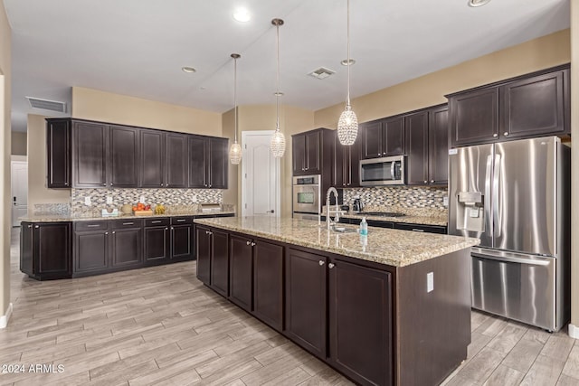 kitchen featuring a center island with sink, light stone countertops, decorative light fixtures, dark brown cabinetry, and stainless steel appliances