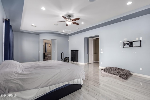 bedroom with ensuite bathroom, a raised ceiling, ceiling fan, and light hardwood / wood-style floors