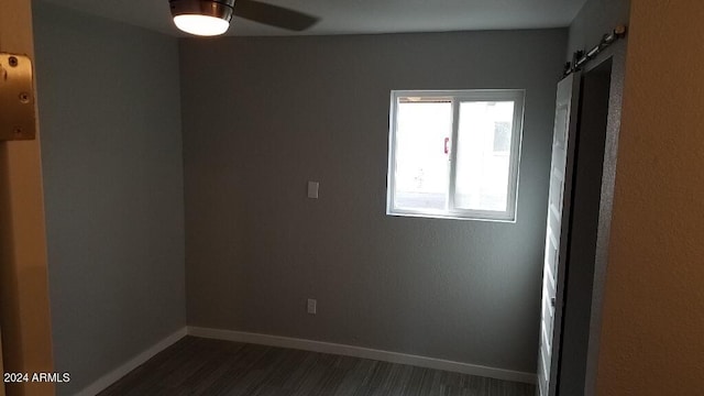 spare room with ceiling fan, a barn door, and dark hardwood / wood-style flooring