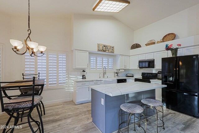 kitchen featuring a center island, black appliances, white cabinets, hanging light fixtures, and light hardwood / wood-style floors