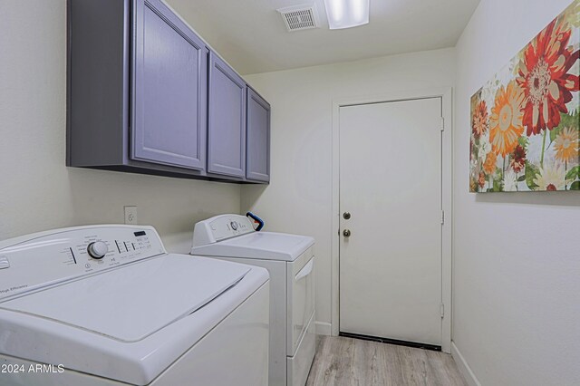 clothes washing area featuring washing machine and dryer, cabinets, and light hardwood / wood-style floors