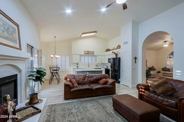 living room featuring light hardwood / wood-style flooring, ceiling fan with notable chandelier, vaulted ceiling, and sink