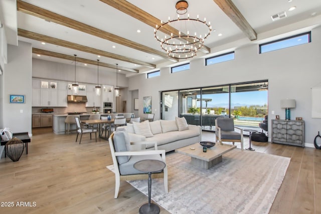 living room with baseboards, light wood-style floors, a towering ceiling, beamed ceiling, and a chandelier