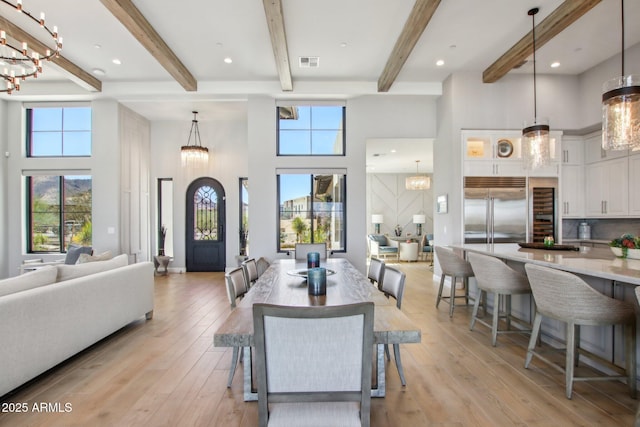 dining room featuring light wood finished floors, visible vents, an inviting chandelier, and a towering ceiling