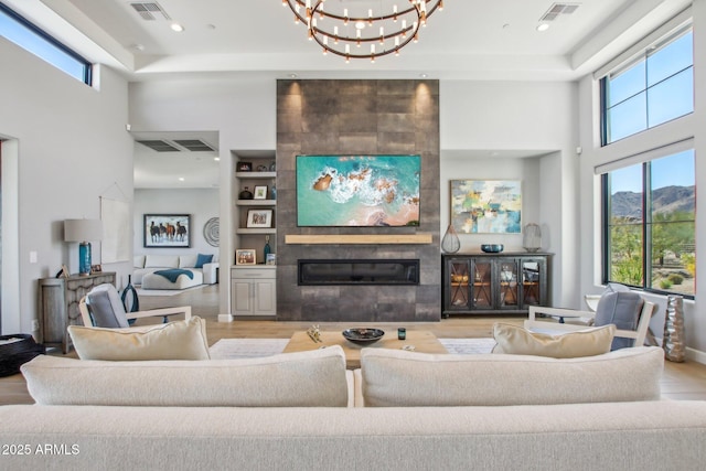 living room with built in features, visible vents, a notable chandelier, and a towering ceiling