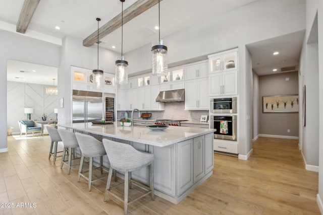 kitchen with under cabinet range hood, beam ceiling, appliances with stainless steel finishes, and tasteful backsplash