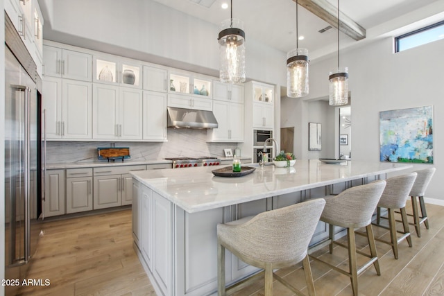 kitchen featuring under cabinet range hood, tasteful backsplash, light wood-style flooring, and white cabinets