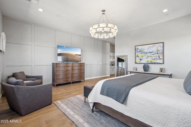 bedroom featuring a decorative wall, recessed lighting, light wood-style floors, and a chandelier