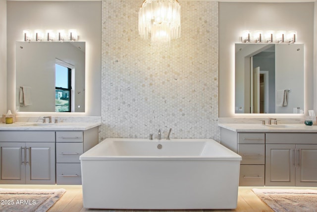 full bath with a sink, two vanities, an accent wall, and wallpapered walls