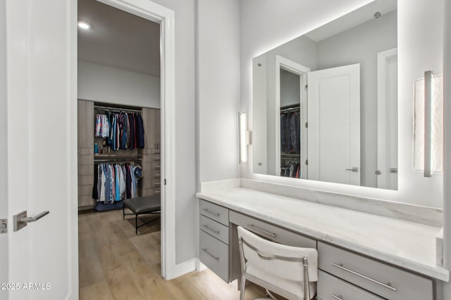 bathroom with a walk in closet, vanity, and wood finished floors