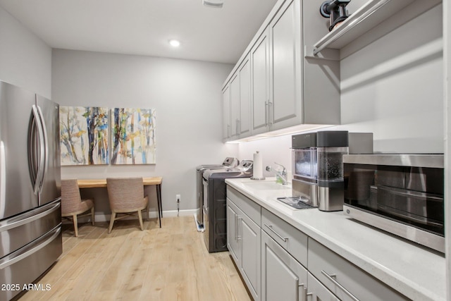 washroom featuring baseboards, light wood-type flooring, laundry area, washer and dryer, and a sink