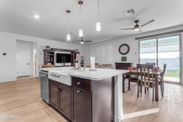 kitchen featuring decorative light fixtures, light wood-type flooring, stainless steel dishwasher, plenty of natural light, and an island with sink