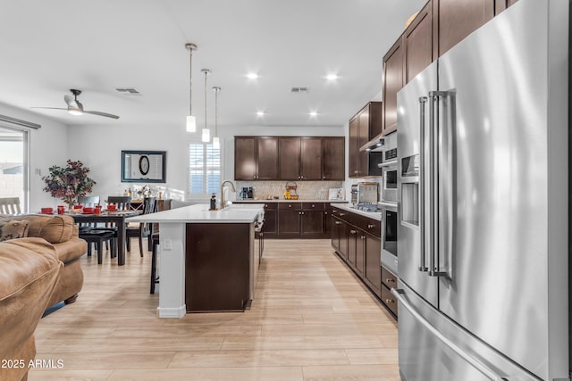 kitchen with pendant lighting, a breakfast bar, appliances with stainless steel finishes, backsplash, and a center island with sink