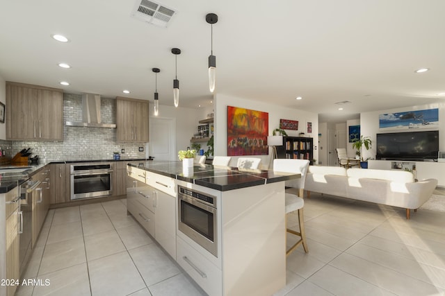 kitchen featuring backsplash, oven, wall chimney range hood, hanging light fixtures, and a kitchen bar