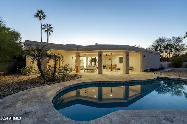 pool at dusk featuring outdoor lounge area, ceiling fan, and a patio area