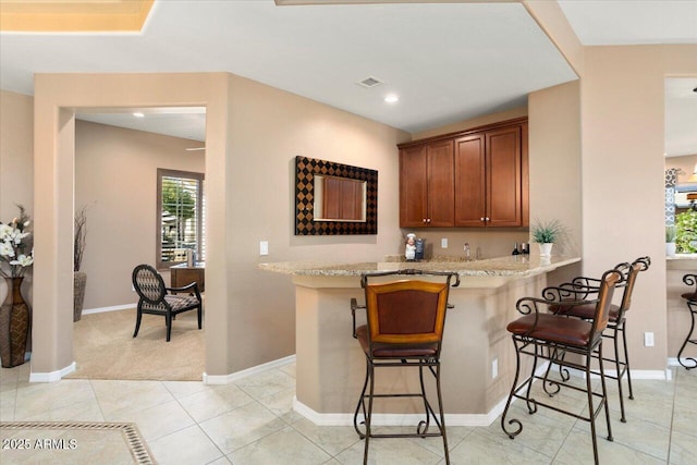 kitchen with light stone countertops, light tile patterned floors, a kitchen breakfast bar, and kitchen peninsula