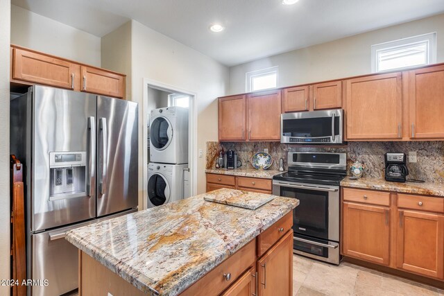 kitchen featuring decorative backsplash, stainless steel appliances, stacked washer / drying machine, and a kitchen island