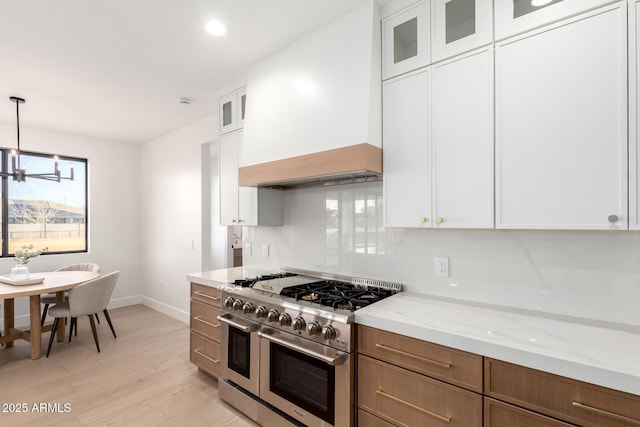 kitchen featuring range with two ovens, light stone counters, custom range hood, light wood-style floors, and white cabinets