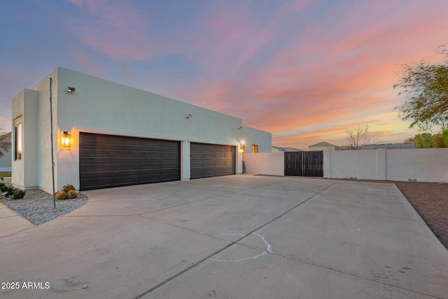 exterior space featuring concrete driveway, fence, a gate, and stucco siding