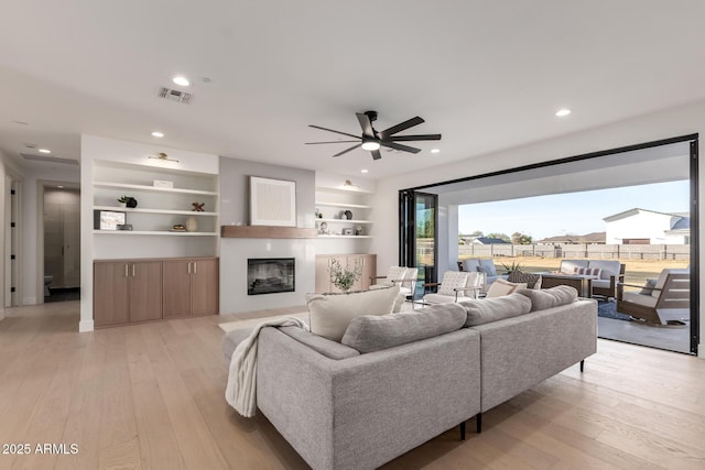 living room featuring recessed lighting, a glass covered fireplace, visible vents, and light wood-style floors