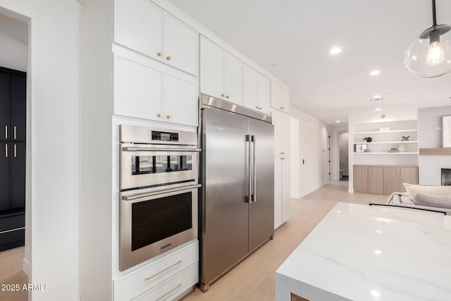 kitchen with light wood finished floors, white cabinets, appliances with stainless steel finishes, light stone counters, and open floor plan