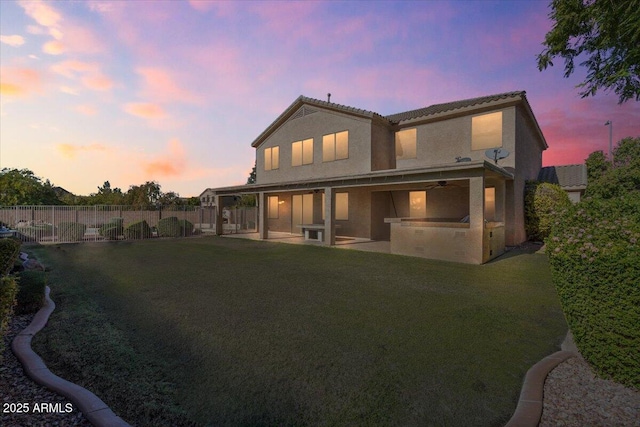 back of property at dusk with a yard, a fenced backyard, stucco siding, and a patio