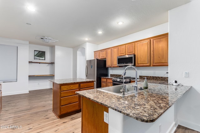 kitchen with dark stone counters, kitchen peninsula, light hardwood / wood-style flooring, sink, and appliances with stainless steel finishes