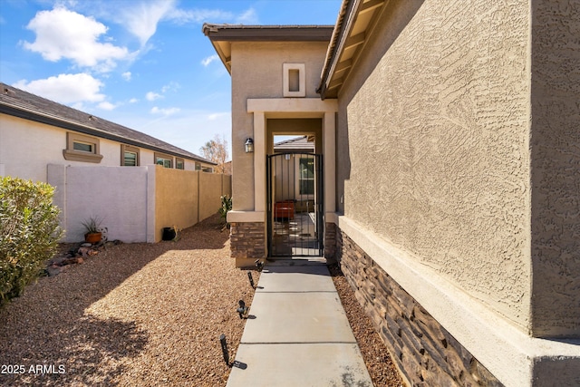 property entrance with a gate, fence, and stucco siding