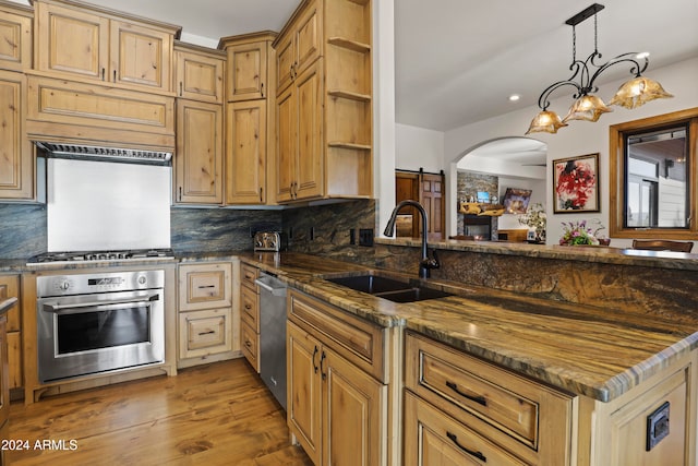 kitchen featuring sink, hanging light fixtures, stainless steel appliances, dark stone countertops, and hardwood / wood-style flooring