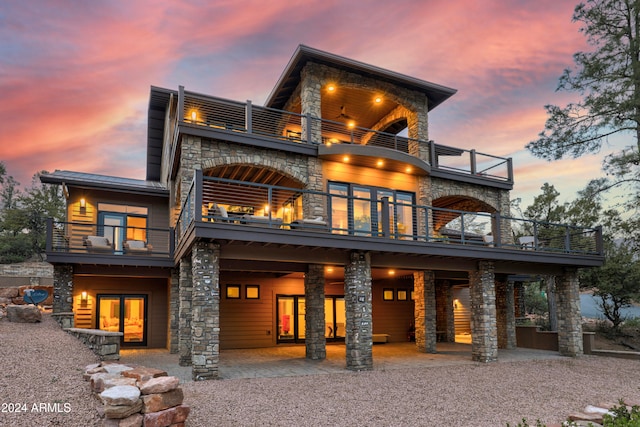 back house at dusk featuring a patio and a balcony